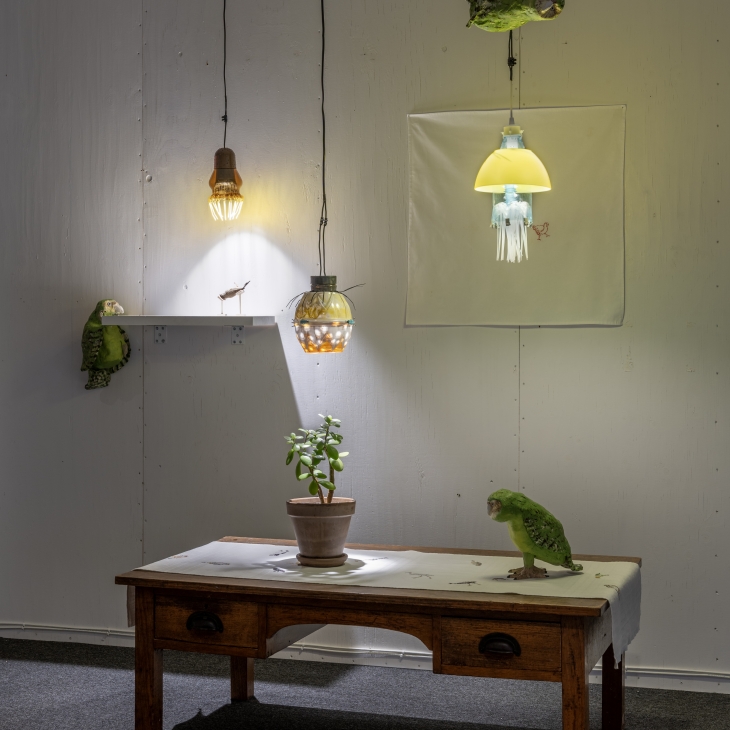 Embroidered tablecloth, plastic electric lights, wooden table, clay figurines, bird cup, potted plant by Ulvi Haagensen